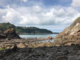 A view of an Ilfracombe beach through a gap in the rocks with people playing and walking on the rocks near a rock pool